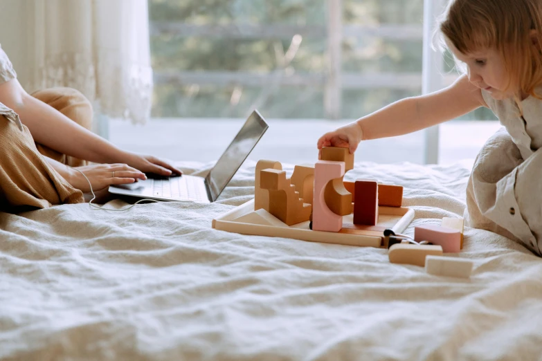 a little girl sitting on top of a bed next to a laptop, pexels contest winner, interactive art, building blocks, couple on bed, wooden art toys, sleek hands