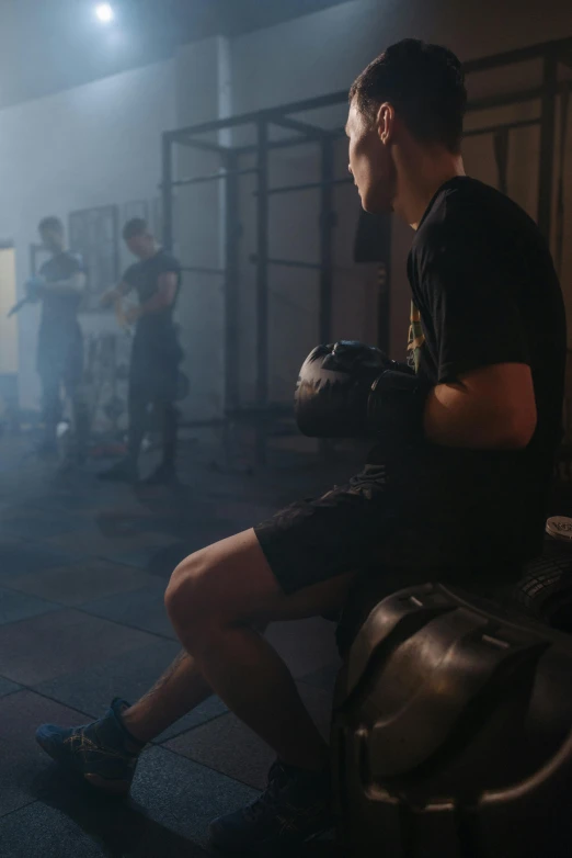 a man sitting on a bench in a gym, by Adam Marczyński, pexels contest winner, realism, choreographed fight scene, smoke filled room, golden gloves, ( ( theatrical ) )