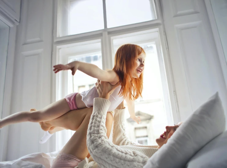 a woman laying on top of a man on a bed, pexels contest winner, arabesque, young redhead girl in motion, with a kid, bottom angle, the girl on a windowsill