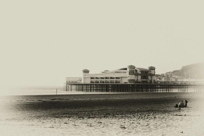 a black and white photo of people on the beach, inspired by William Twigg-Smith, bauhaus, seaside victorian building, old sepia photography, hazy, pavilion