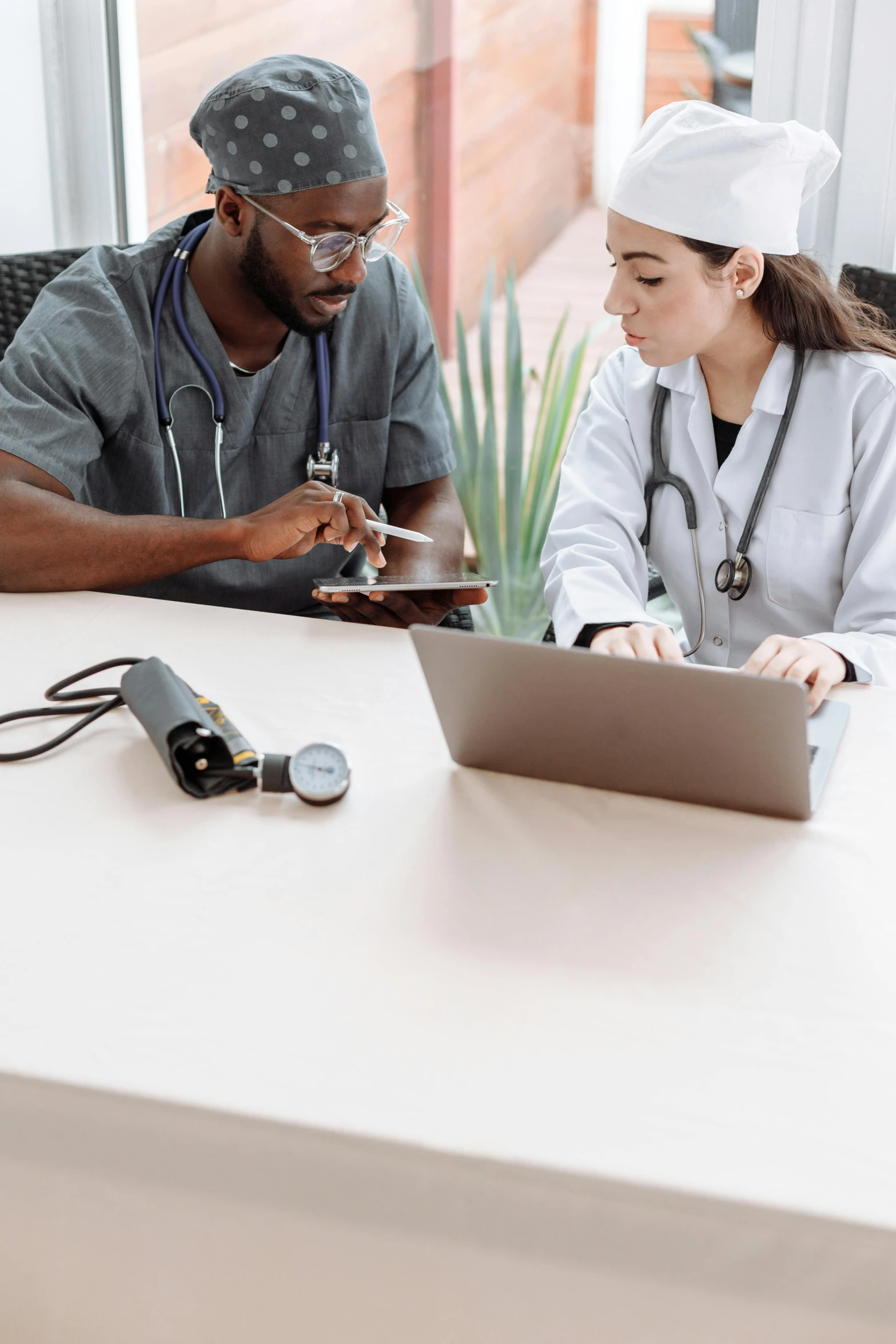 a couple of people sitting at a table with a laptop, with a stethoscope, varying ethnicities, thumbnail, grey