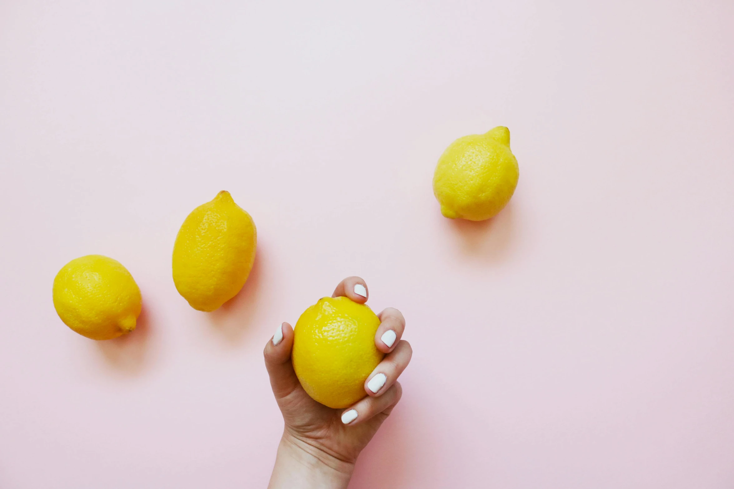 a woman's hand holding a lemon on a pink background, by Carey Morris, trending on unsplash, peeled lemons, background image, group photo, on a pale background