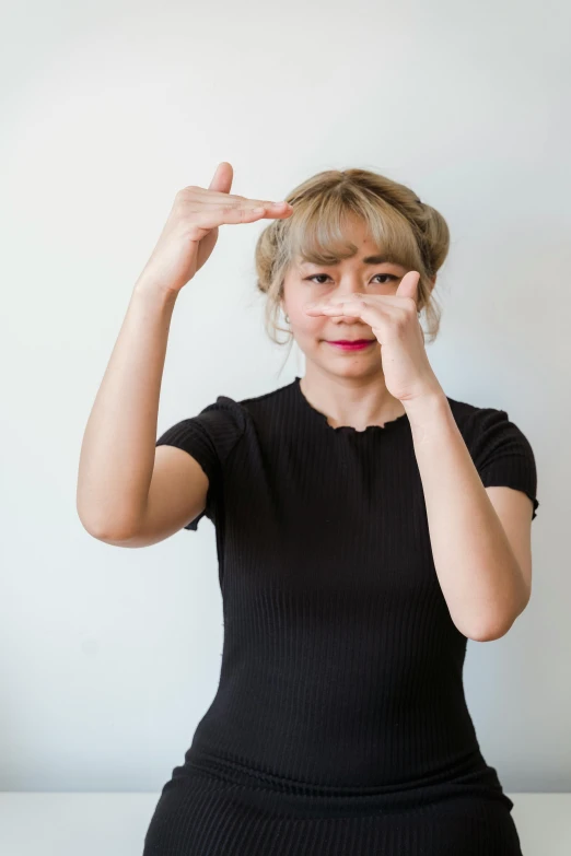 a woman sitting on top of a white table, an album cover, inspired by Kim Jeong-hui, trending on unsplash, hands shielding face, south east asian with round face, saluting, wearing a black shirt