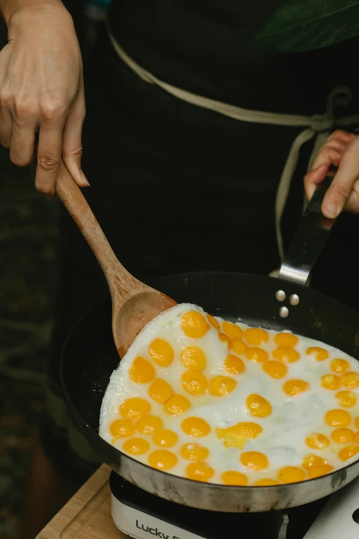 a person cooking eggs in a skillet on a stove, by Jessie Algie, trending on unsplash, raw egg yolks, nature outside, made of glazed, lots of mozzarella balls