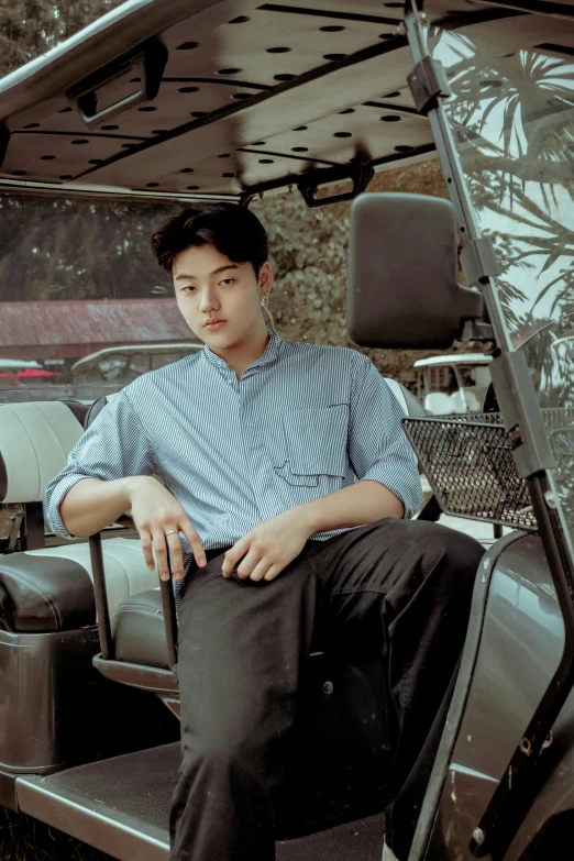 a man sitting on the back of a golf cart, an album cover, inspired by Zhang Han, unsplash, realism, confident pose, wearing a light blue shirt, serious look, 18 years old