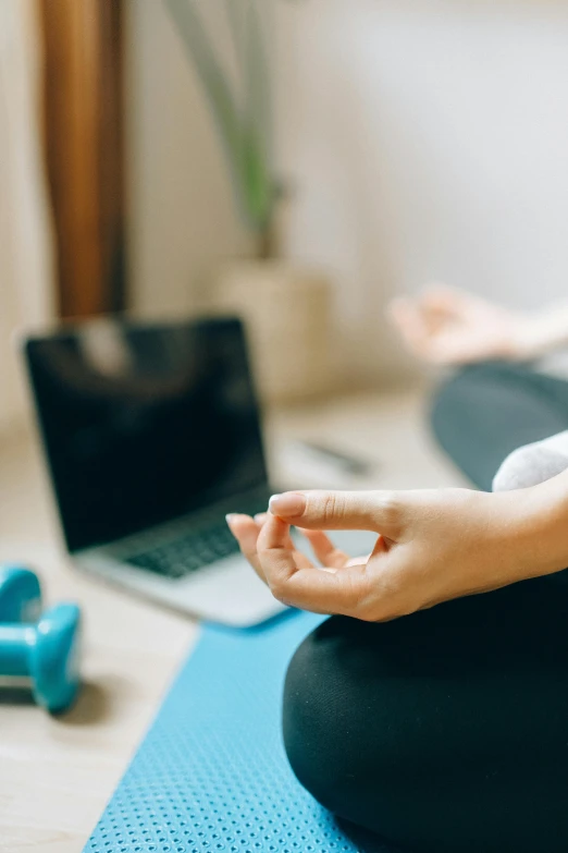 a woman sitting on a yoga mat in front of a laptop, figure meditating close shot, in the center of the image, zoomed in, middle shot