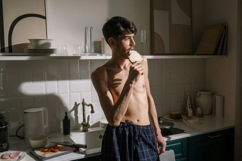 a man standing in a kitchen next to a sink, by Elsa Bleda, pexels contest winner, hyperrealism, eating garlic bread, model with attractive body, 14 yo berber boy, tall and slender