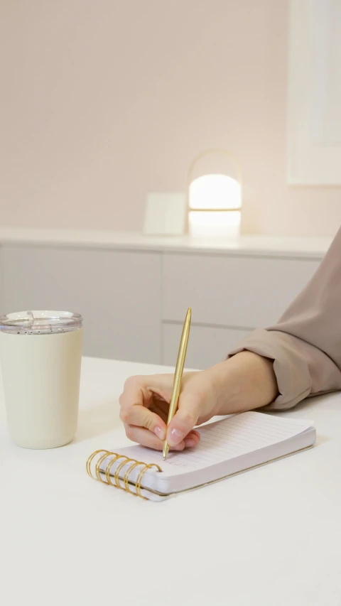 a woman sitting at a table writing on a notebook, light and space, japanese collection product, beige, multiple lights, milk