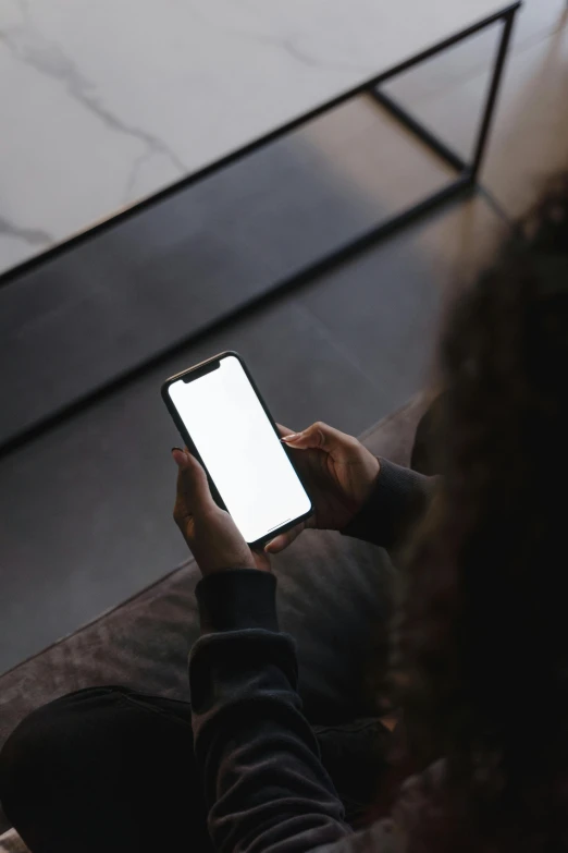 a woman sitting on a couch holding a cell phone, trending on pexels, hypermodernism, dark. no text, corporate phone app icon, dark-skinned, rectangle