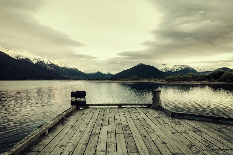 a dock on a lake with mountains in the background, unsplash, hurufiyya, vintage photo, new zeeland, album cover, whistler