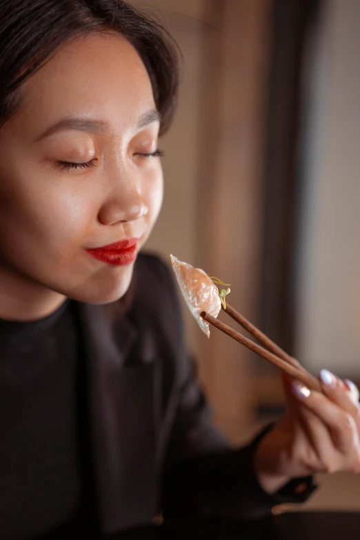 a woman eating a piece of food with chopsticks, inspired by Ruth Jên, wearing professional makeup, warm glow, profile image, black