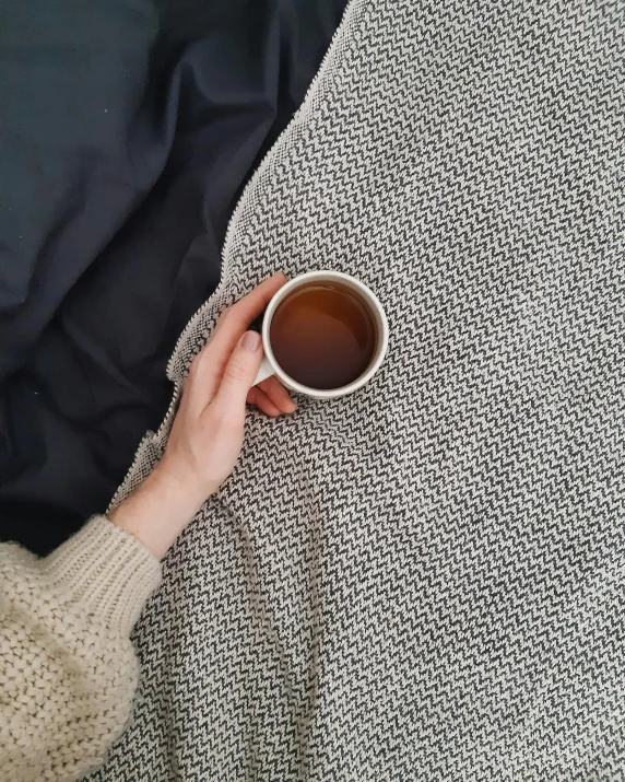 a person laying on a bed holding a cup of coffee, black wool sweater, birdseye view, wearing nanotech honeycomb robe, real trending on instagram image