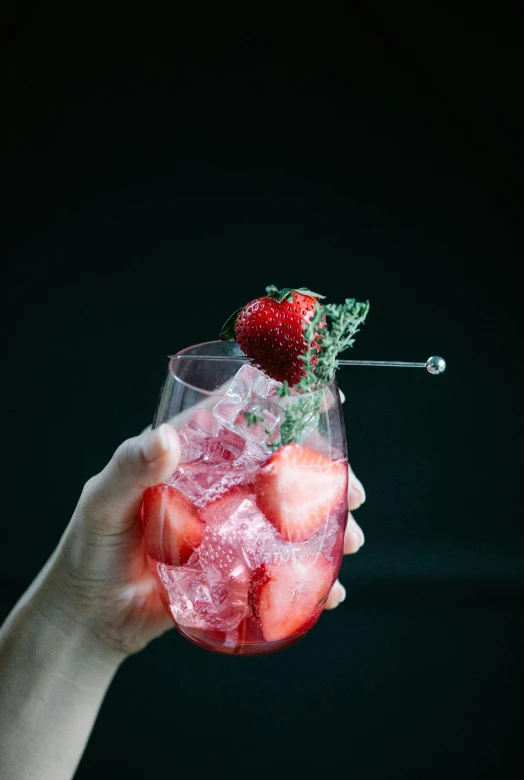 a person holding a glass filled with ice and strawberries, inspired by Wlodzimierz Tetmajer, cocktail bar, ivy's, with a black background, sparkling