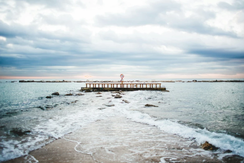 a man riding a surfboard on top of a sandy beach, unsplash, near a jetty, caulfield, frozen sea, in the evening