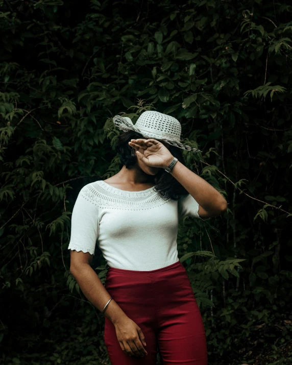 a woman wearing a white top and red pants, pexels contest winner, green hat, biophilia mood, queer woman, shy and demure