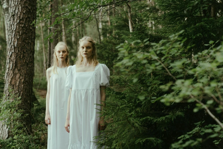 two women in white dresses standing in the woods, inspired by Vanessa Beecroft, unsplash, hammershøi, live action movie, looking towards camera, mid shot photo