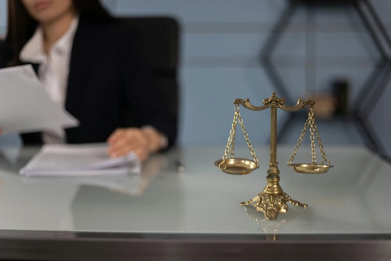 a woman sitting at a desk with a scale of justice in front of her, pexels contest winner, hurufiyya, hovering indecision, instagram post, holding a staff, background image