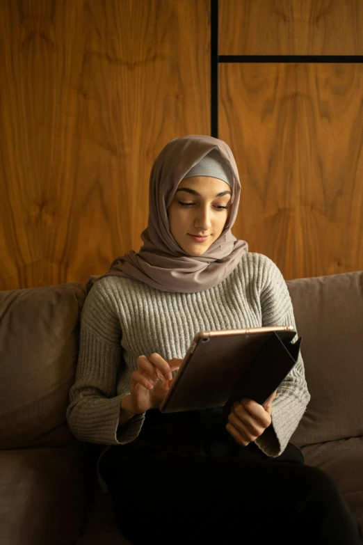 a woman sitting on a couch reading a book, inspired by Maryam Hashemi, hurufiyya, gaming, medium head to shoulder shot, islamic, holding notebook