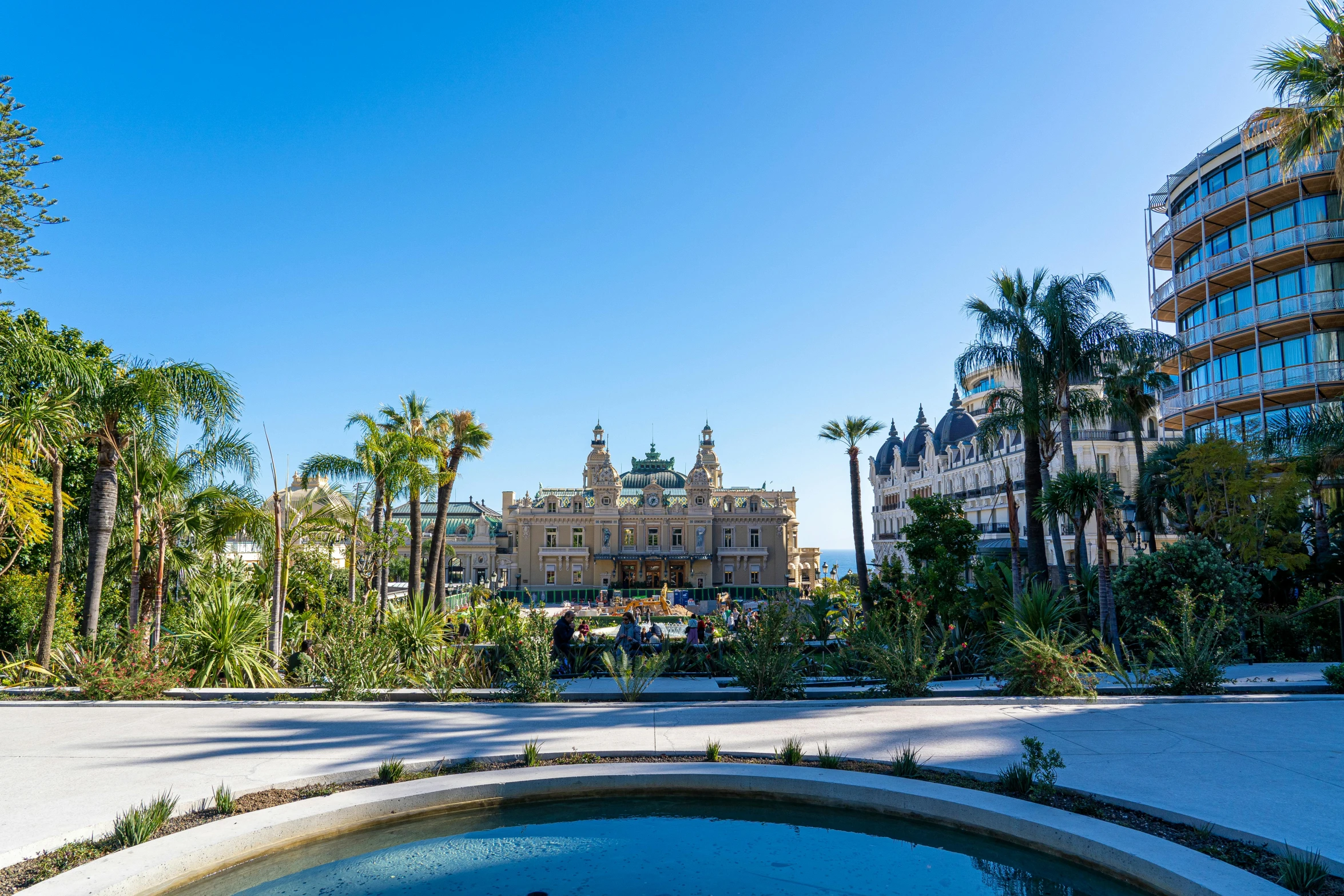 a pool surrounded by palm trees in front of a large building, pexels contest winner, art nouveau, monaco, buildings carved out of stone, a green, flowers around
