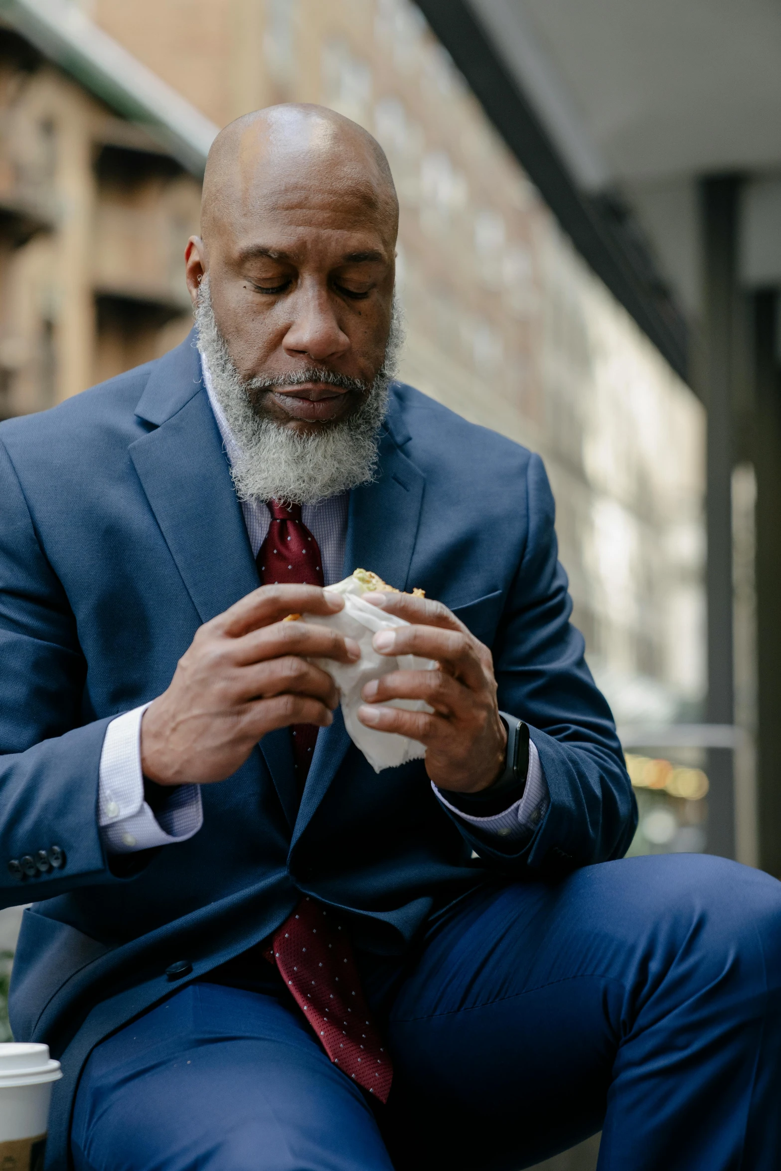 a man sitting on a bench eating a sandwich, a photo, by Dan Frazier, pexels contest winner, renaissance, wearing a worn out suit, bald head and white beard, jemal shabazz, fried chicken