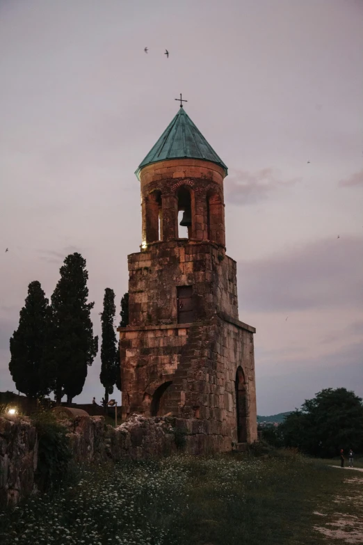 a tall tower sitting on top of a lush green hillside, an album cover, inspired by Arthur Sarkissian, pexels contest winner, romanesque, evening lights, orthodox, exterior view, multi - coloured