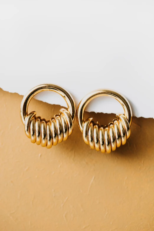 a pair of gold earrings sitting on top of a piece of paper, by Julia Pishtar, trending on pexels, swirly tubes, plain background, a pair of ribbed, round doors