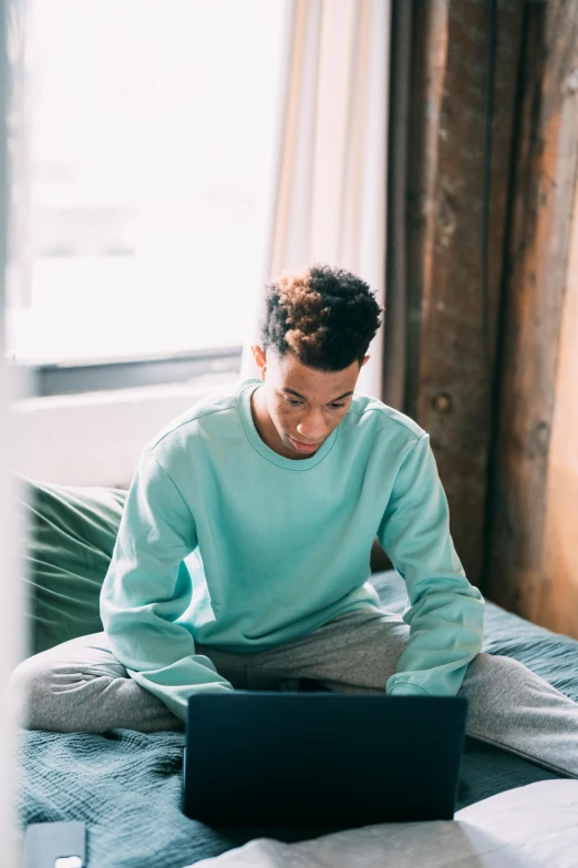 a man sitting on a bed using a laptop, trending on pexels, renaissance, with teal clothes, black teenage boy, pastel green, sitting on couch