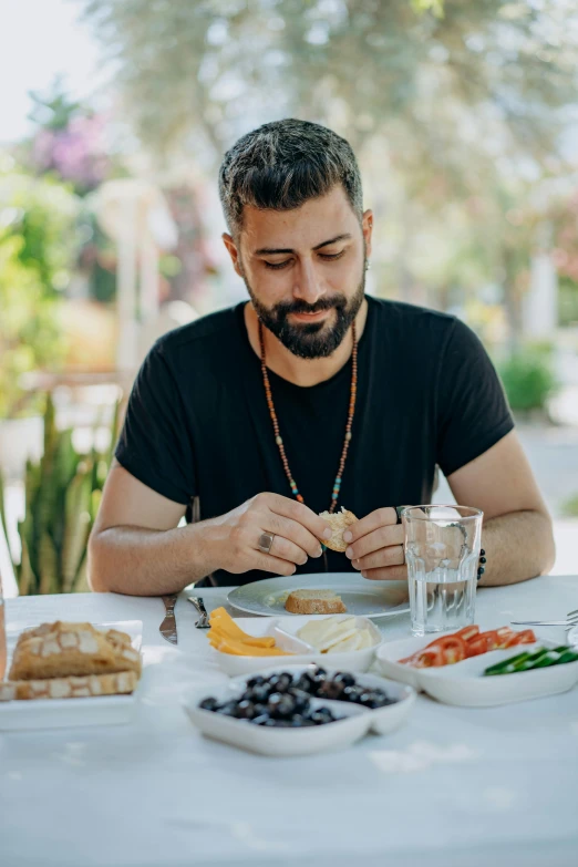 a man sitting at a table with a plate of food, inspired by Nadim Karam, pexels contest winner, young greek man, man with beard, breakfast, al fresco