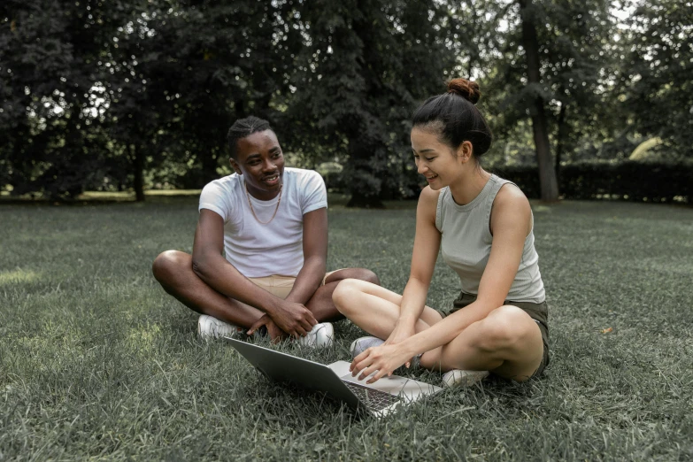 a couple of people sitting in the grass with a laptop, wearing a tank top and shorts, mix of ethnicities and genders, trending ，, supportive