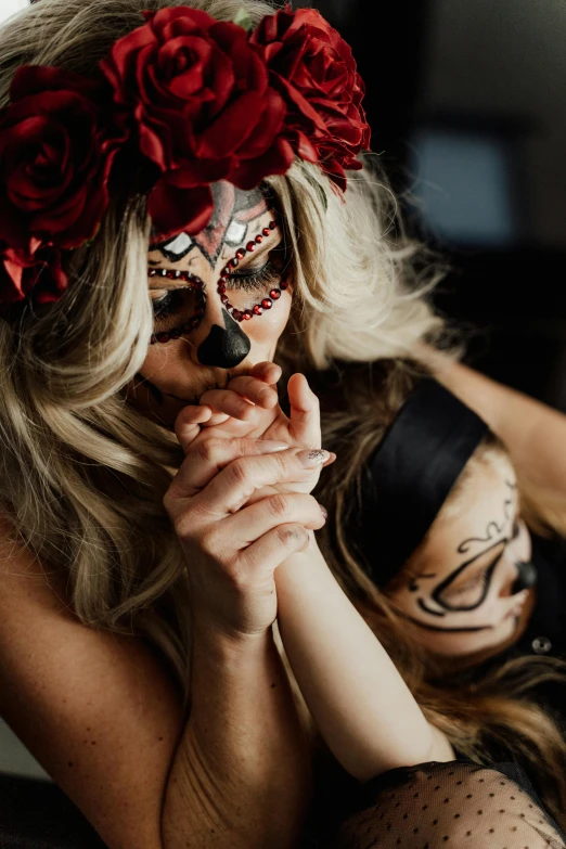 a woman sitting on top of a bed next to another woman, a tattoo, trending on pexels, conceptual art, dia de los muertos makeup, hands shielding face, black and red colour palette, motherly