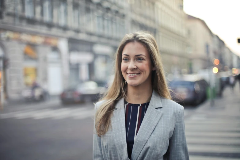 a woman standing in the middle of a street, a portrait, by Emma Andijewska, in a business suit, smiling young woman, profile image, thumbnail