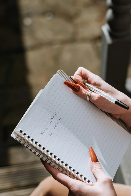 a woman sitting on a bench holding a notebook and pen, pexels contest winner, hidden message, jen atkin, high angle close up shot, on a notebook page