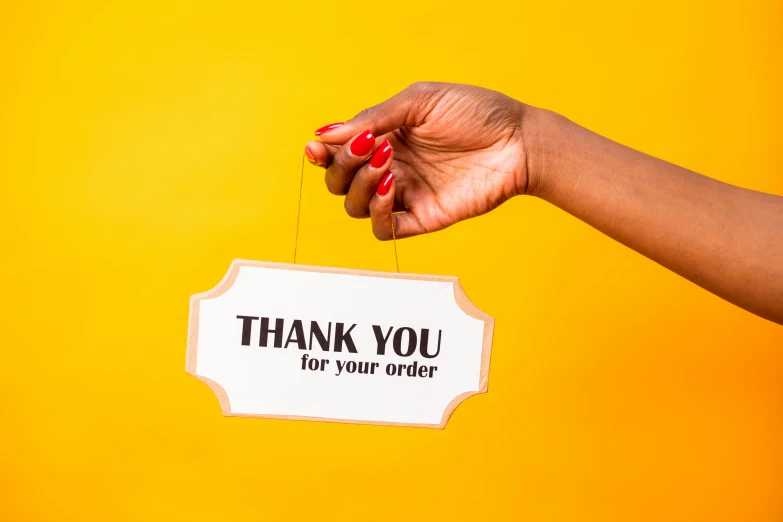 a woman holding a sign that says thank you for your order, by Julia Pishtar, yellow, high quality product photography, close-up of thin soft hand, maria borges