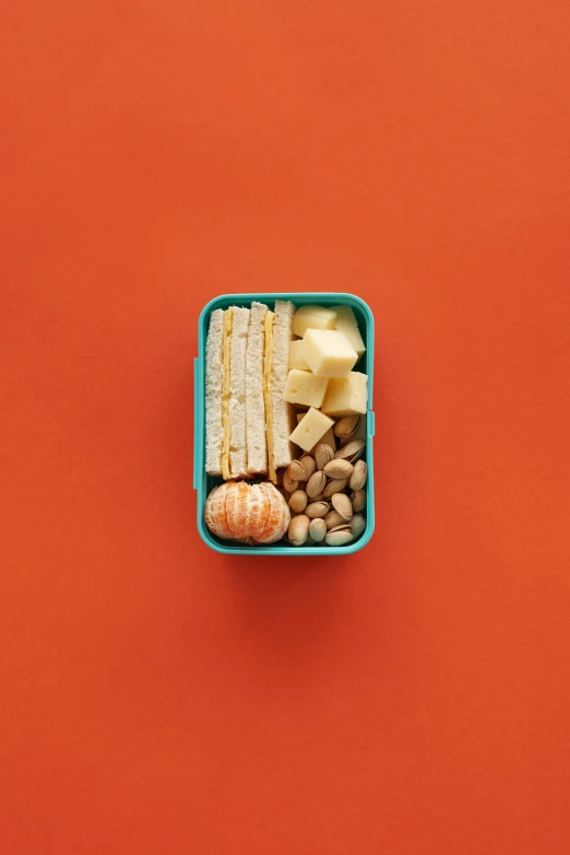 a close up of a container of food on a red surface, by Alison Geissler, pexels, hypermodernism, made of cheese, cyan and orange, nut, knolling