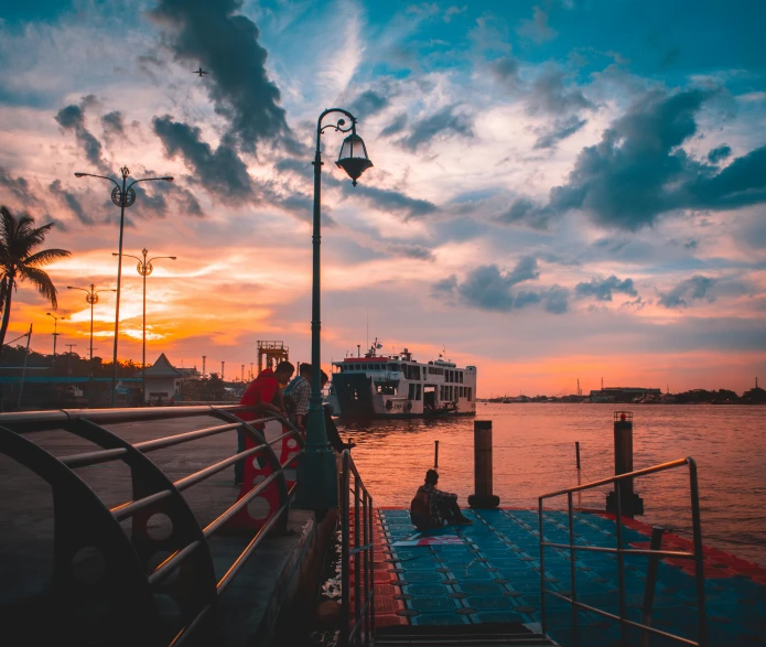 a group of people standing on top of a pier next to a body of water, pexels contest winner, romanticism, boat with lamp, interior of staten island ferry, sunset and big clouds behind her, venice at dusk