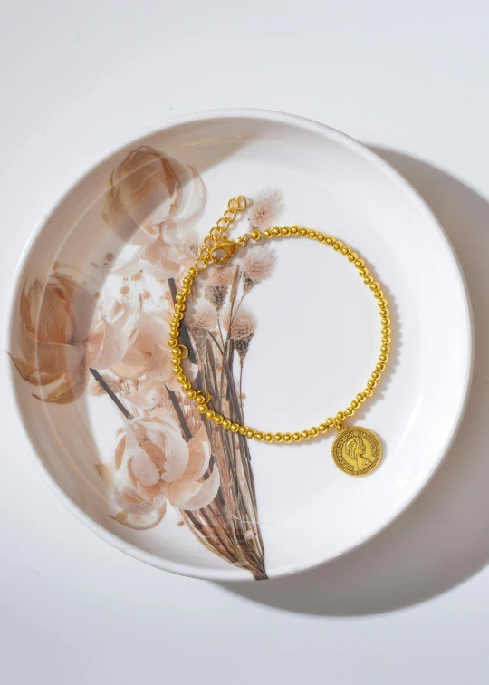 a gold bracelet sitting on top of a white plate, a cartoon, inspired by Evert Collier, trending on unsplash, renaissance, beads, textured base ; product photos, coin, yellow