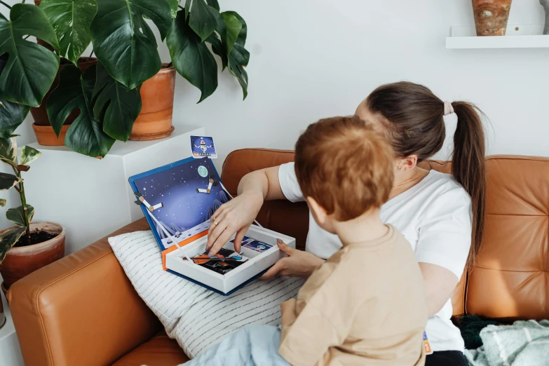 a woman and a child sitting on a couch, a storybook illustration, by Julia Pishtar, pexels contest winner, happening, small astronauts, inside its box, product introduction photos, using a macbook