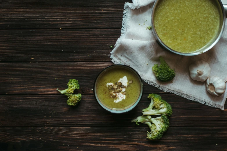 a bowl of soup next to a bowl of broccoli, a portrait, unsplash, wooden, background image, olive green, foil