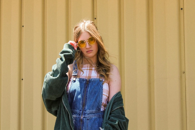 a woman standing in front of a building talking on a cell phone, by Julia Pishtar, trending on pexels, photorealism, wearing overalls, aviator shades, sadie sink, wearing gold glasses