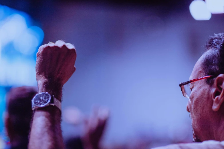 a close up of a person raising their hands, a portrait, by Adam Marczyński, trending on unsplash, wears glasses, watch photo, purple and blue leather, rabbids at a metal concert