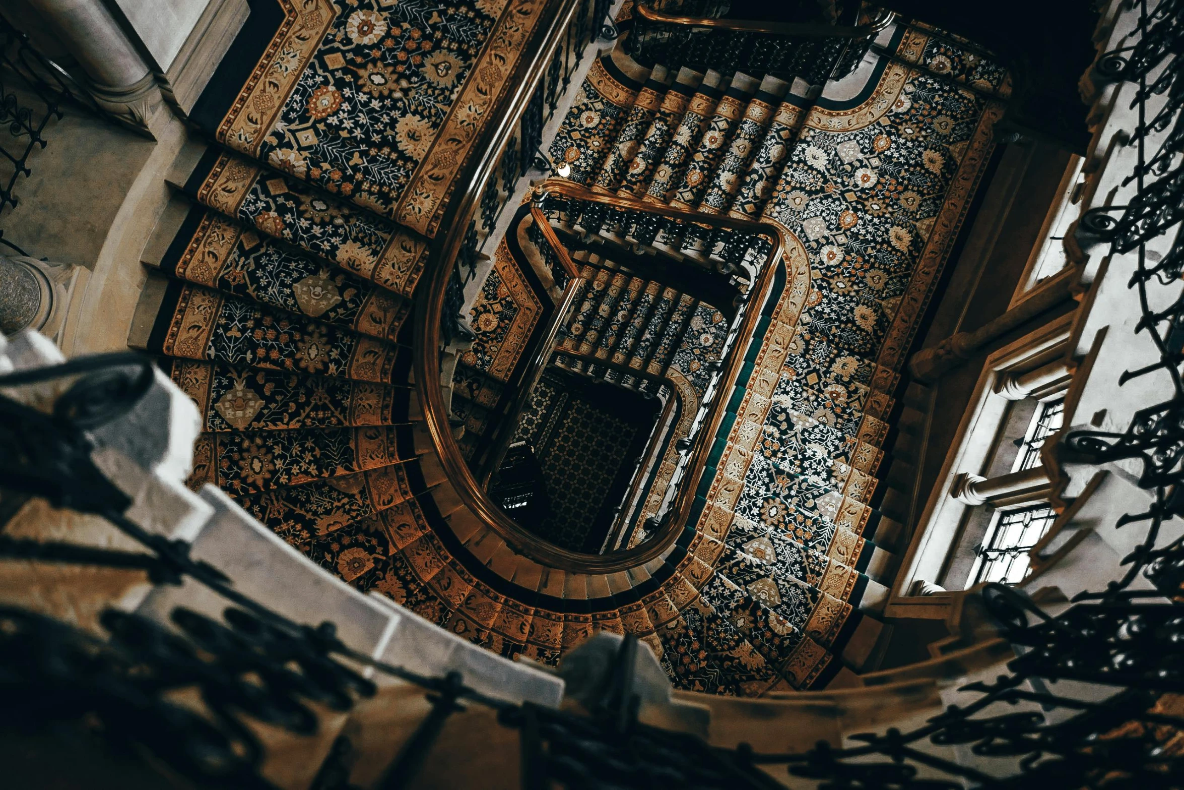 a spiral staircase in the middle of a building, a mosaic, unsplash contest winner, baroque, haunted gothic hotel, patterned clothing, arabic architecture, down there