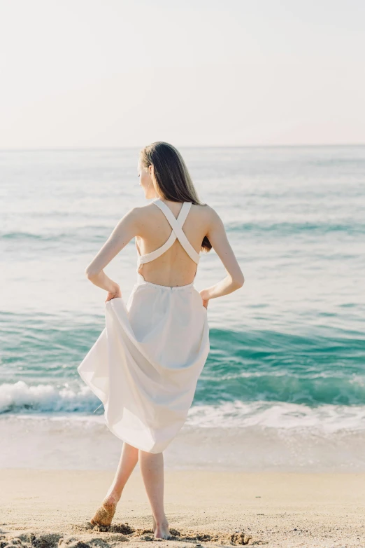 a woman in a white dress standing on a beach, unsplash, renaissance, open back dress, clean and pristine design, back view »