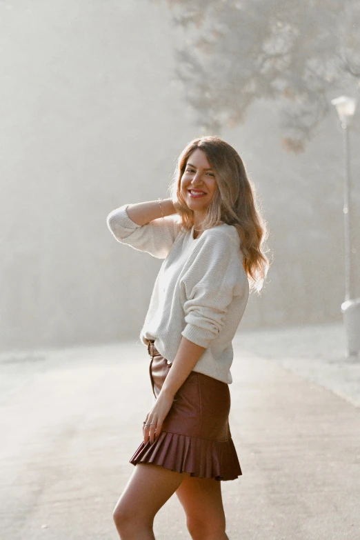 a woman standing in the middle of a road, inspired by Johann Christian Brand, trending on pexels, renaissance, wearing a white sweater, in a glowing skirt, elegant smiling pose, brown sweater