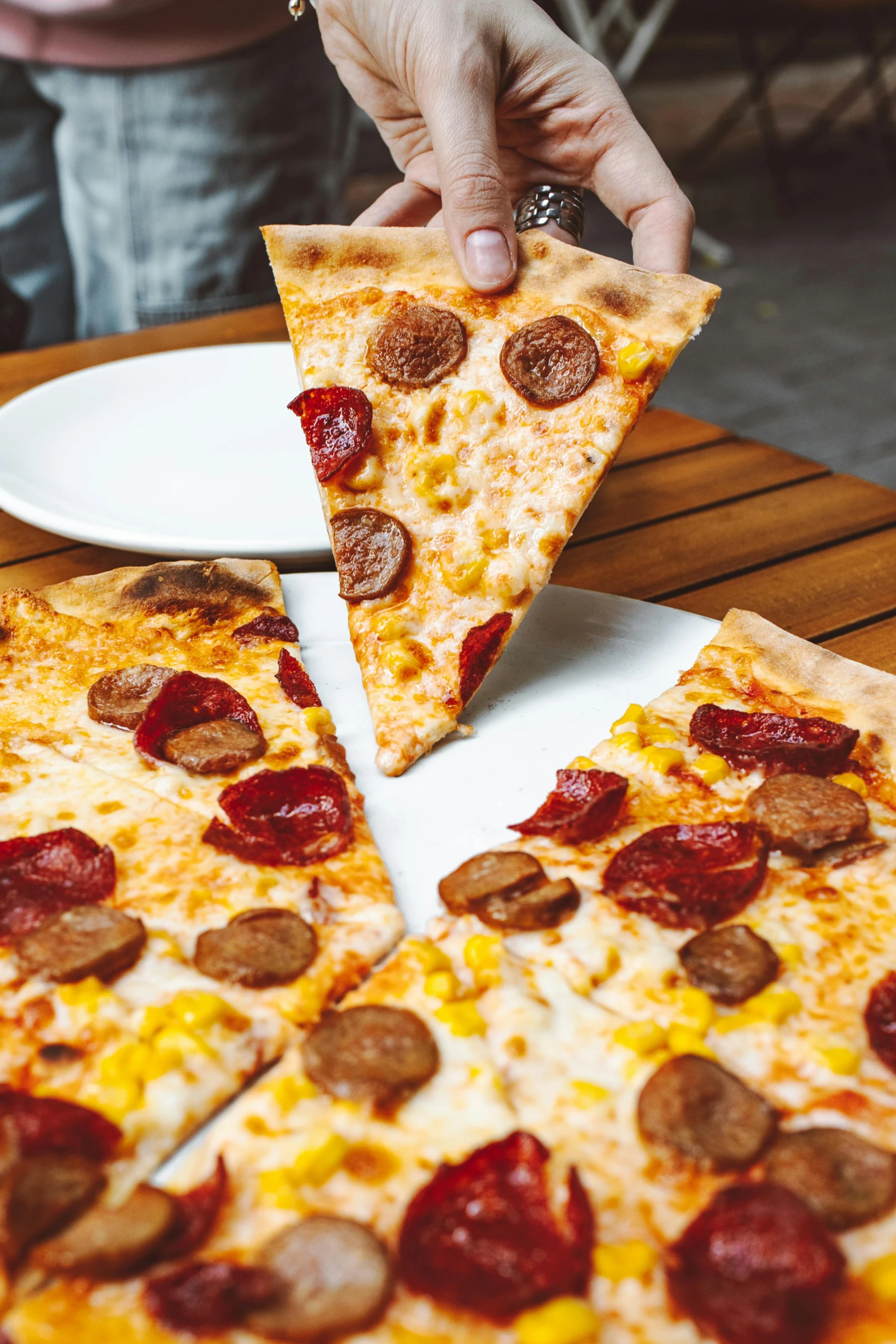 a person taking a slice of pizza from a table, chorizo sausage, tall angle, one on each side, sparky