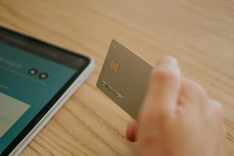 a person holding a credit card next to a cell phone, a digital rendering, by Adam Marczyński, pexels contest winner, square, white and teal metallic accents, a wooden, information