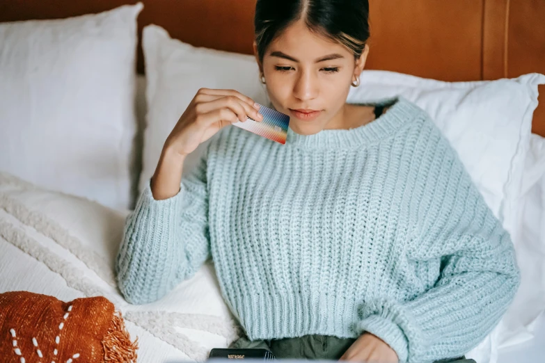 a woman sitting on a bed using a laptop, trending on pexels, sweater, chewing on a graphic card, south east asian with round face, with teal clothes