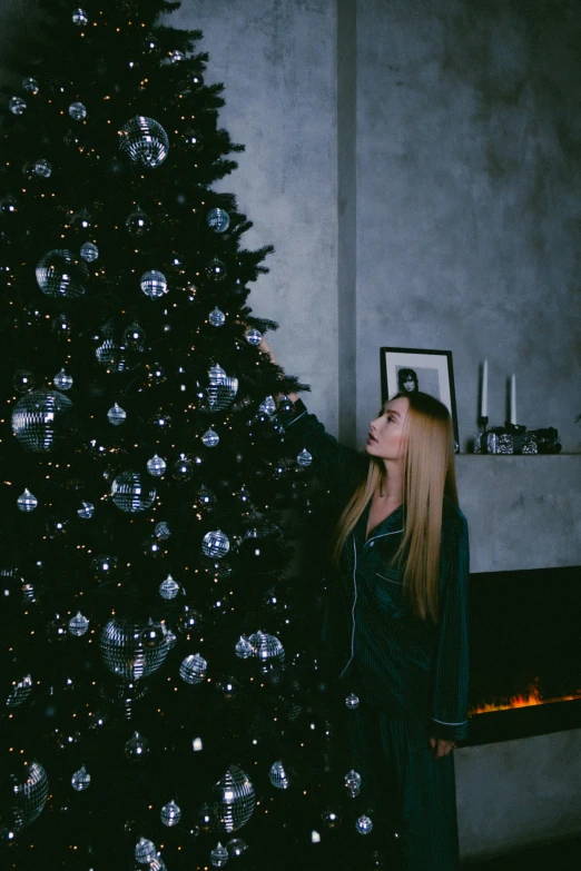 a woman standing in front of a christmas tree, inspired by Elsa Bleda, pexels contest winner, realism, black, decoration around the room, with long blond hair, gif