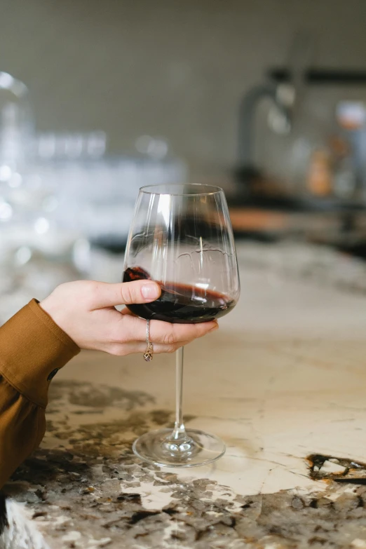 a close up of a person holding a glass of wine, large glasses, brown, deep colour, hands on counter