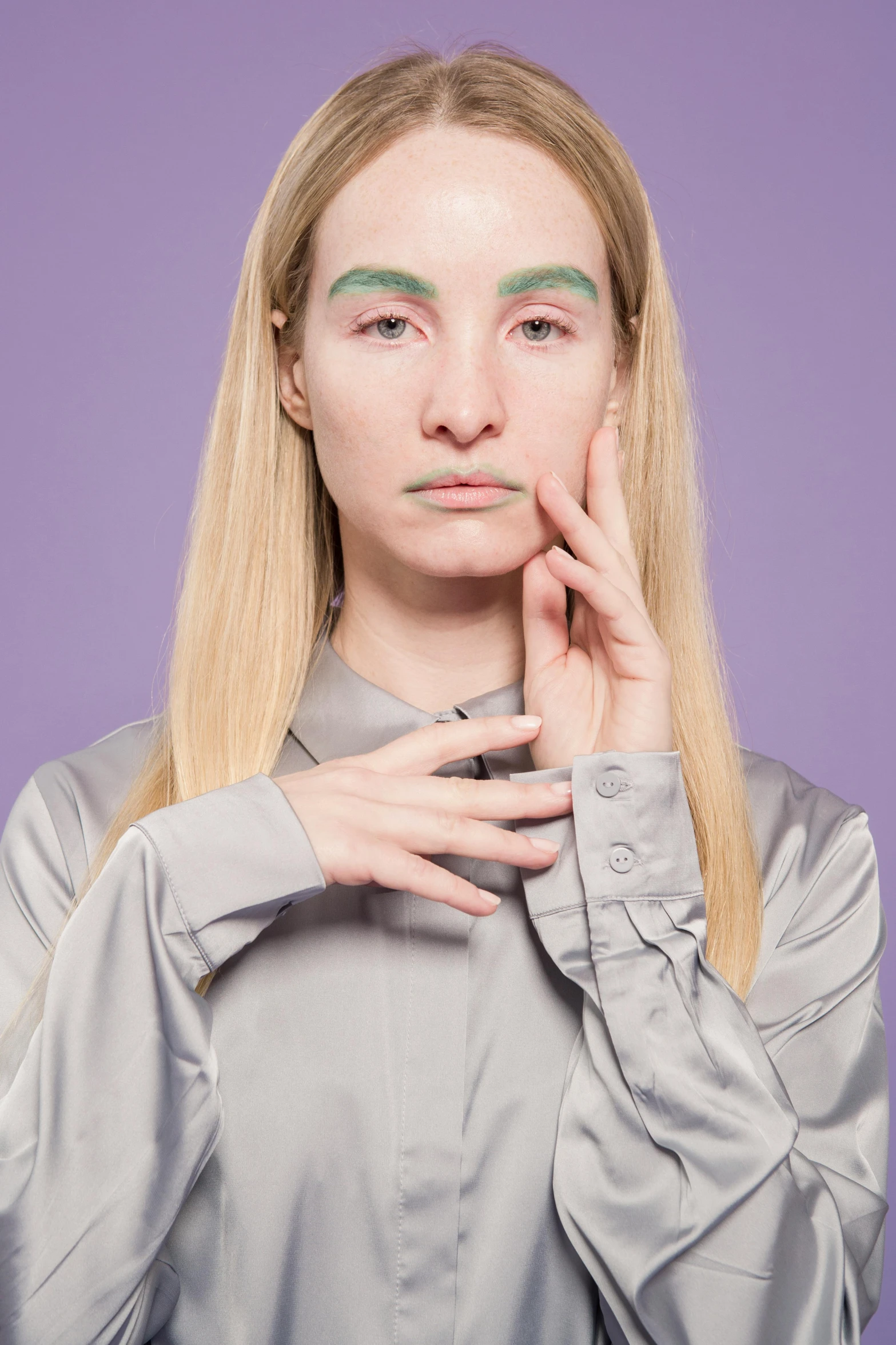 a woman with long blonde hair posing in front of a purple background, inspired by Maud Naftel, skin painted with green, hands on face, on grey background, genderless