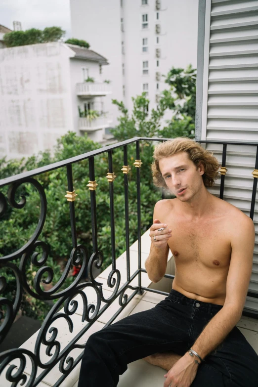 a man sitting on a balcony smoking a cigarette, inspired by Nan Goldin, trending on unsplash, curly blond hair, beefcake pose, buenos aires, low quality photo